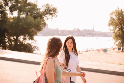 Girlfriends talking while walking by beach during summer