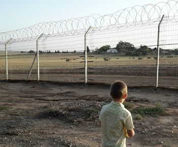 Rear view of boy standing on field against sky