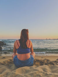 Rear view of woman sitting on beach against clear sky