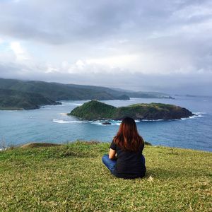 Rear view of woman sitting on green mountain by sea