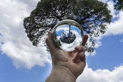 Low angle view of hand holding crystal ball against sky