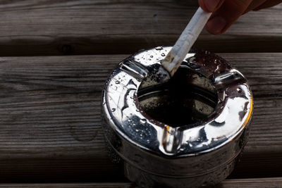 Close-up of hand holding cigarette in ashtray on table