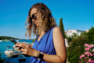 Young woman using mobile phone against clear blue sky