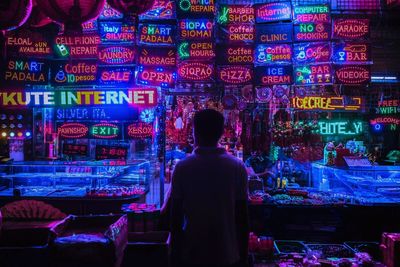 Rear view of man standing against illuminated lights