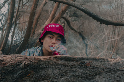 Portrait of young woman looking away against tree trunk