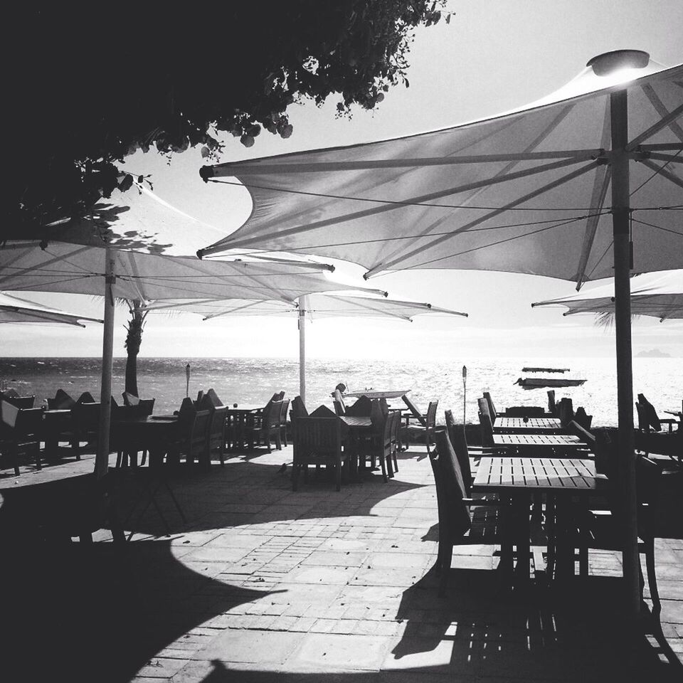 sky, sea, water, sunshade, chair, sunlight, parasol, incidental people, shadow, built structure, leisure activity, outdoors, beach, beach umbrella, table, umbrella, vacations, day, street light