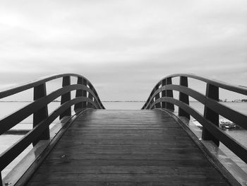 Wooden footbridge over sea against sky