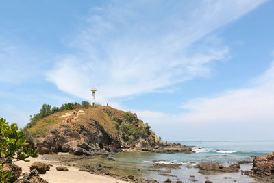 Lighthouse on beach by sea against sky