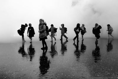 People standing on wet beach against clear sky