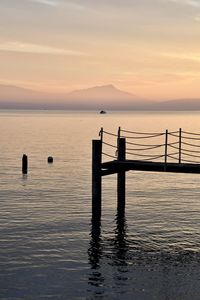 Silhouette wooden post in sea against sky during sunset