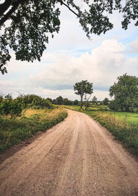 Dirt road amidst field against sky