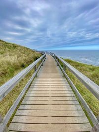 Wooden boardwalk leading towards sea against sky