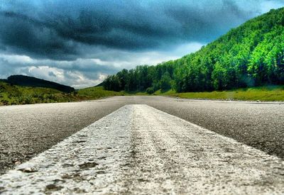 Empty road leading towards mountains against cloudy sky