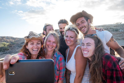 Portrait of smiling young woman using smart phone against sky