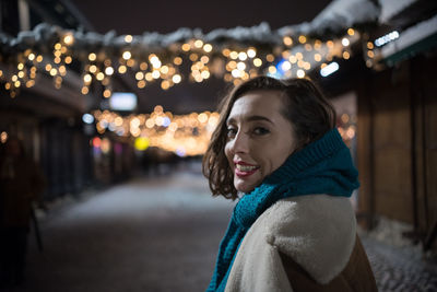 Portrait of smiling woman standing against illuminated lights during winter at night