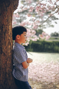 Side view of cute boy standing against tree at park