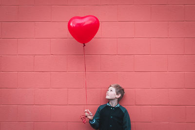 Boy holding balloon while standing against brick wall