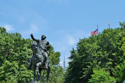 Low angle view of statue against trees against blue sky