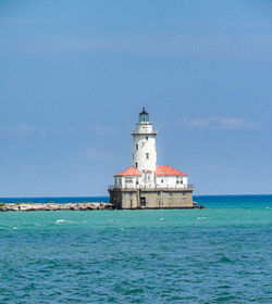 Lighthouse by sea against clear sky