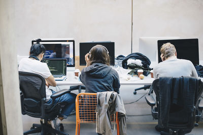 Rear view of programmers using computers at desk in office