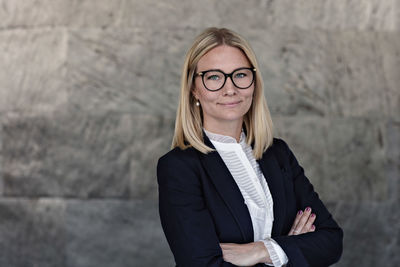 Portrait of businesswoman with arms crossed standing against wall in office