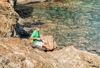 High angle view of man sitting on rock by sea