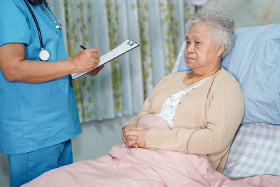 Midsection of woman holding mobile phone while sitting on bed