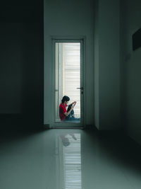 Side view of woman sitting on window