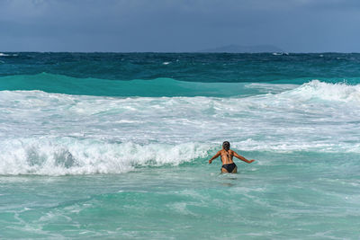 Woman standing in sea with waves on tropical beach with turquoise ocean