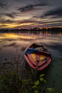 Boat moored at lake against sky during sunset