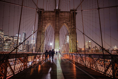 People walking on brooklyn bridge against sky at night