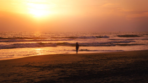 Silhouette woman walking at beach against sky during sunset