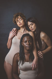 Portrait of women embracing while standing against black background