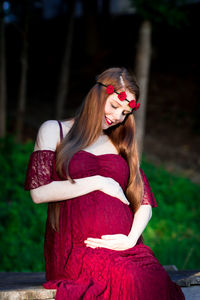 Portrait of pregnant woman sitting on wood outdoors