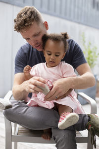 A caucasian father helps his biracial daughter put her shoes on