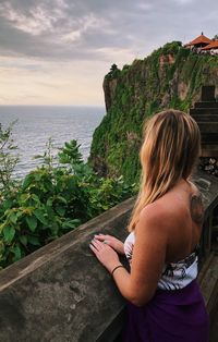 High angle view of woman looking at sea while standing by retaining wall during sunset