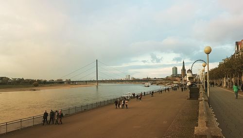 People on bridge over river against sky in city