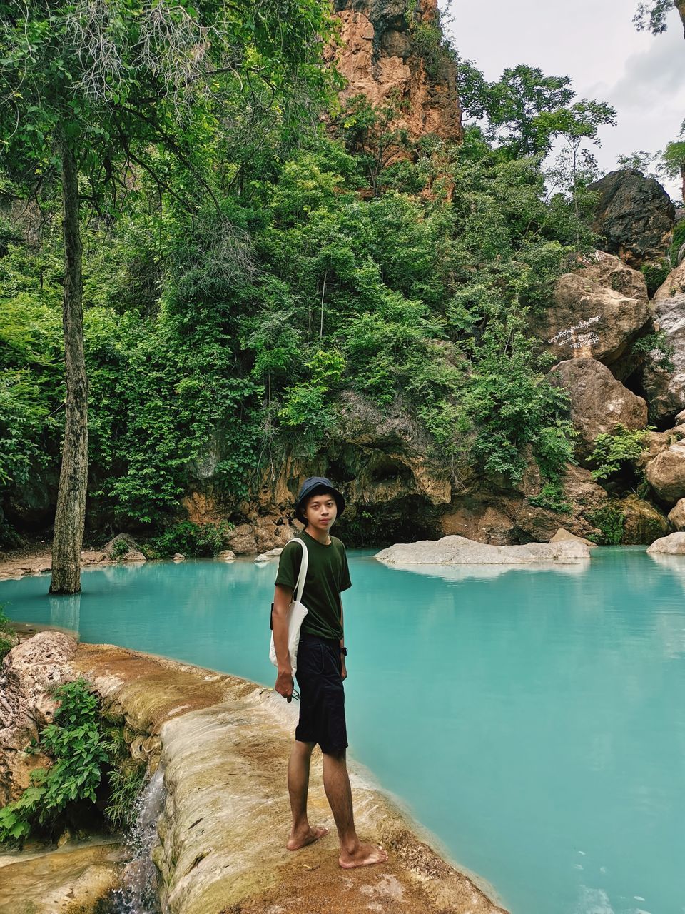 water, tree, one person, plant, nature, full length, leisure activity, beauty in nature, vacation, adult, lifestyles, standing, rock, young adult, trip, scenics - nature, holiday, tranquility, green, day, forest, land, casual clothing, travel, tranquil scene, travel destinations, outdoors, non-urban scene, women, tourism, lake, mountain, clothing, men, body of water, idyllic, front view, relaxation, portrait, environment, fashion, tourist, looking, smiling