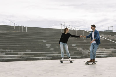 Young couple skateboarding walking near steps