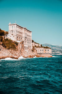 Building by sea against clear blue sky