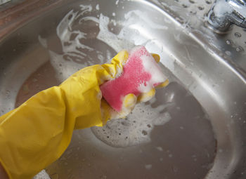 High angle view of cropped hand wearing washing up glove while cleaning sink