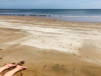 Low section of person on beach against sky