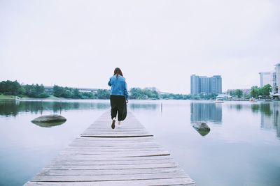 Rear view of woman standing on pier over lake against sky