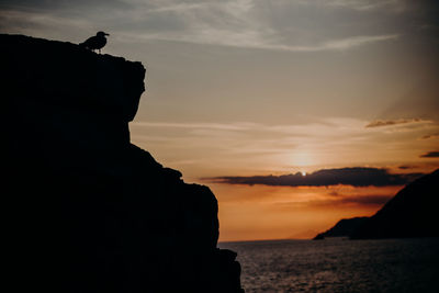 Silhouette rocks on sea against sky during sunset