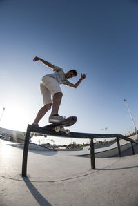 Low section of man jumping on skateboard against clear sky