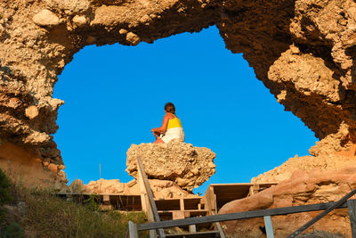 Low angle view of woman sitting on rock against sky