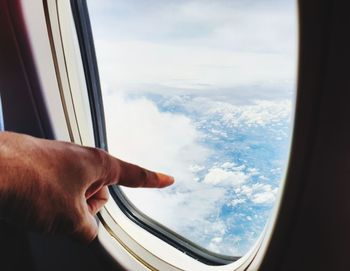 Cropped hand of person gesturing by airplane window