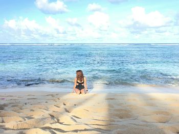 Woman kneeling on sand against sea at beach