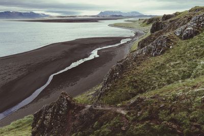 Scenic view of cliff by sea against cloudy sky