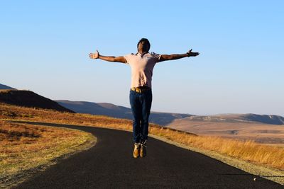 Rear view of man on mid-air landscape against sky with arms stretched